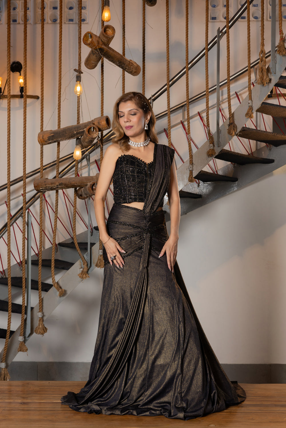 Woman in a black evening gown standing in front of a staircase.